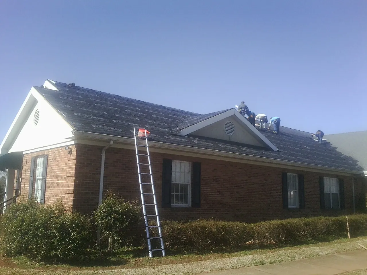 Crew tearing shingles off a brick ranch roof with a ladder set — Metal Roof Repair work by our crew in Letts