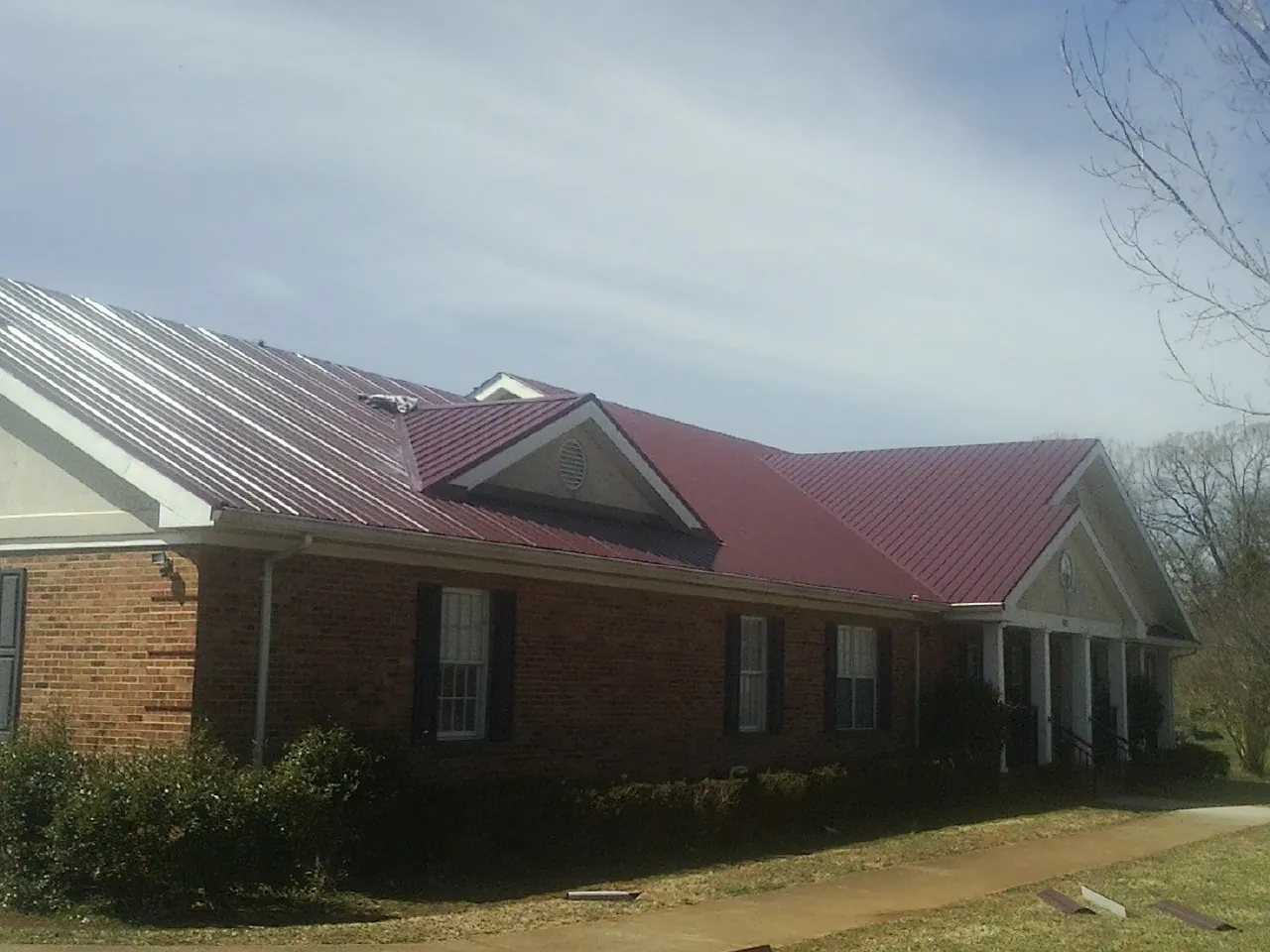 Red metal roof with gabled entries on a long brick building, from a Hail Damage Roof Repair job in Letts