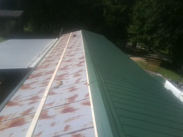 Old rusted panels beside newly installed green metal roofing — Wind Damage Roof Repair by Roofing Brothers in Letts