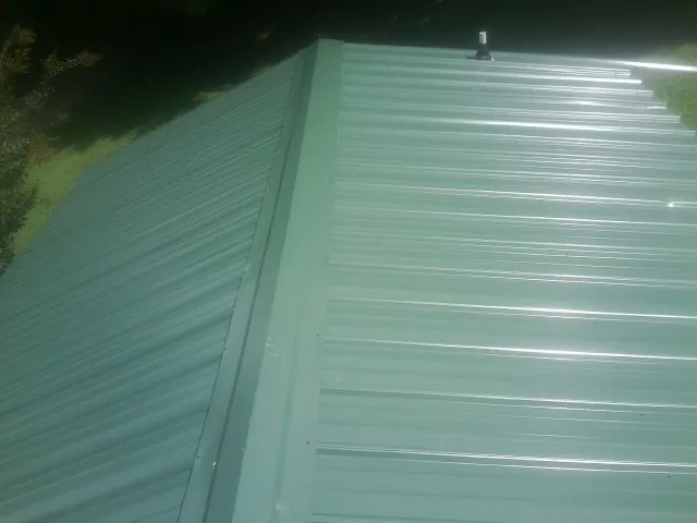 New green metal panels meeting at the ridge of a roof — Flat Roof Repair work by our crew in Letts