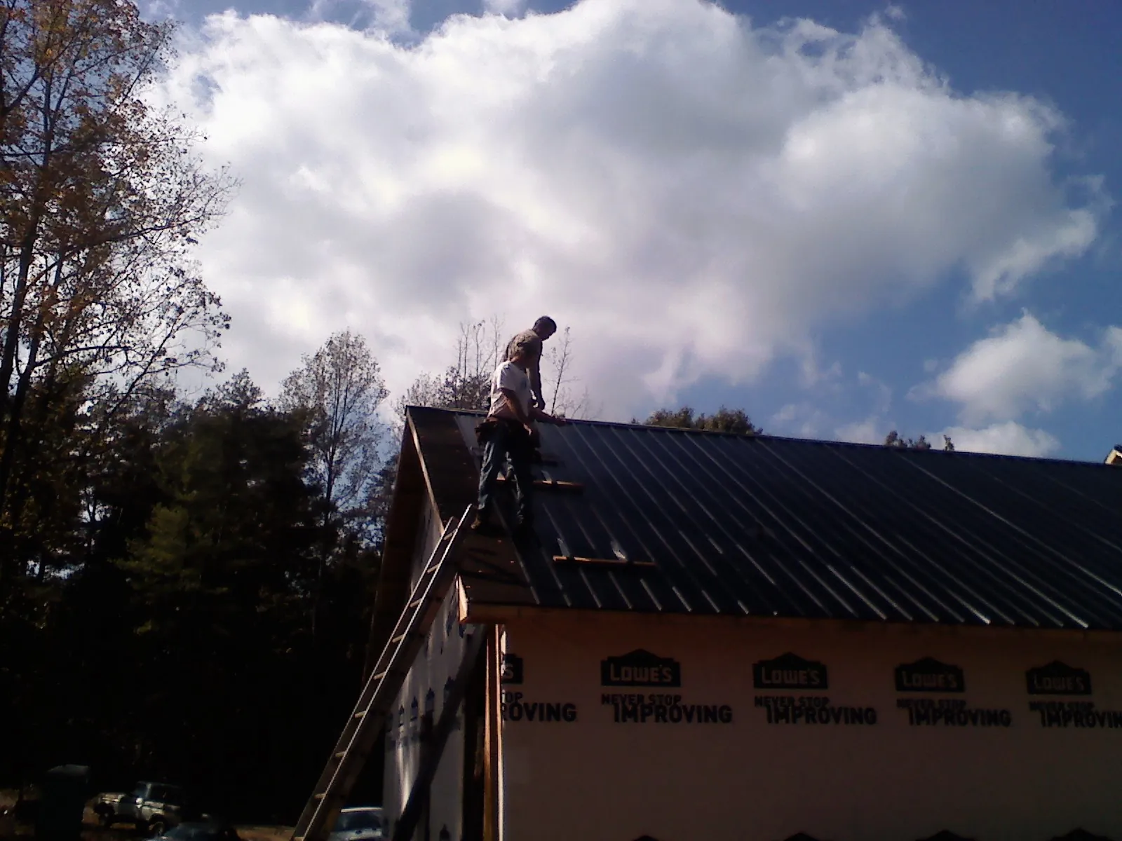 Roofer fastening dark metal panels high against a cloudy sky, from a Roof Inspection job in Letts