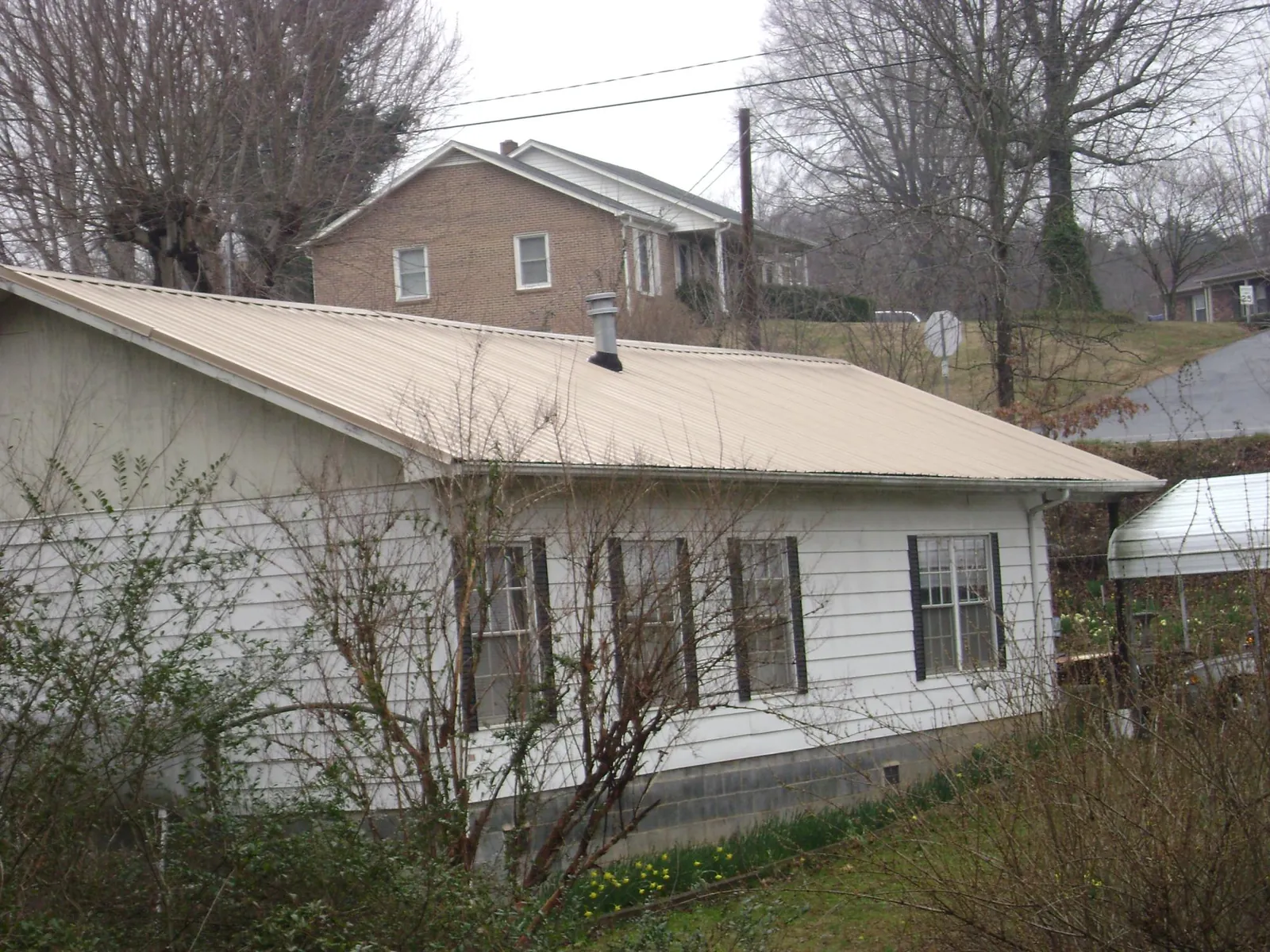 Tan metal roof on a white sided house set into a hillside — Commercial Roofing by Roofing Brothers in Letts